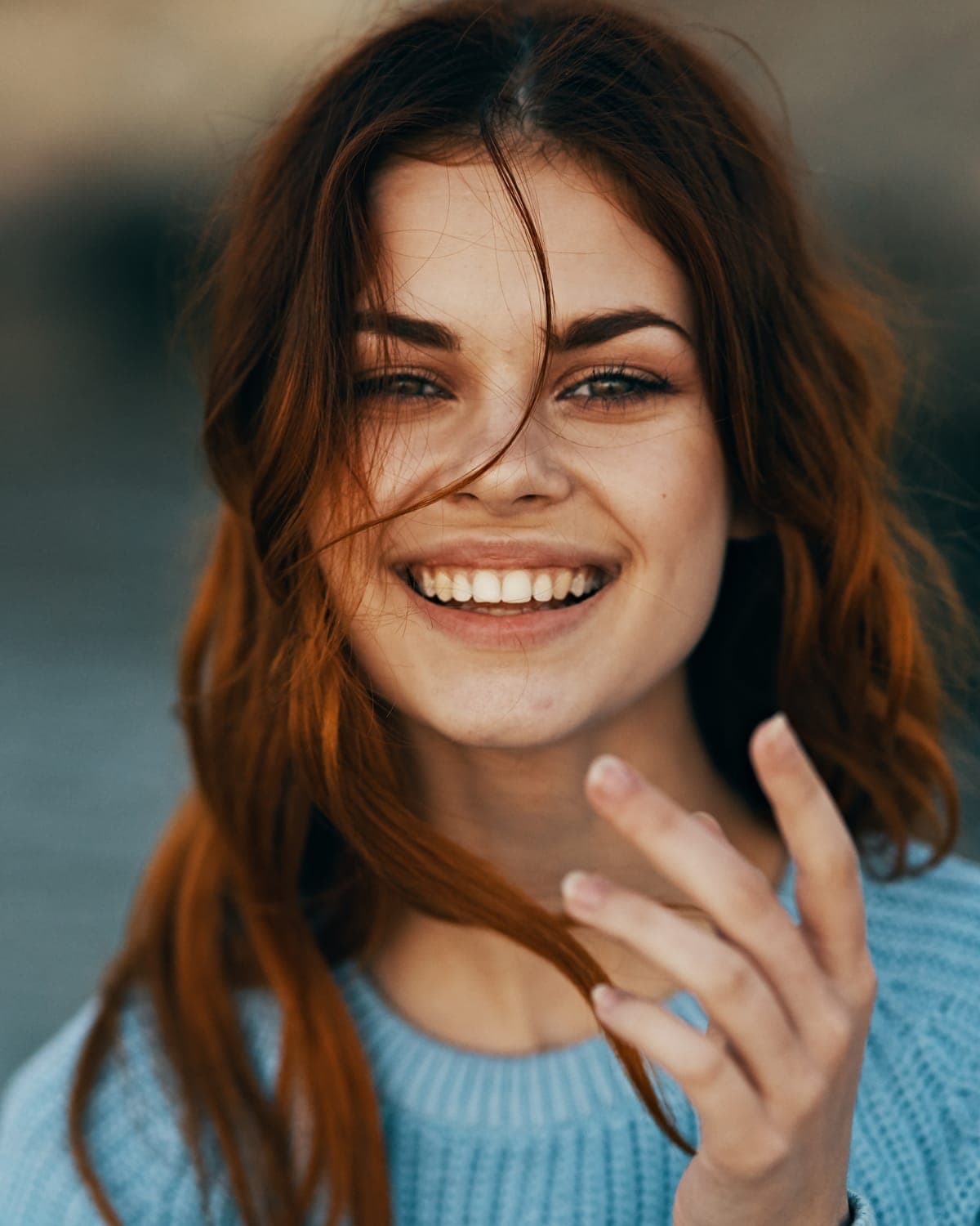 Young woman with auburn hair smiling, her hand near her face