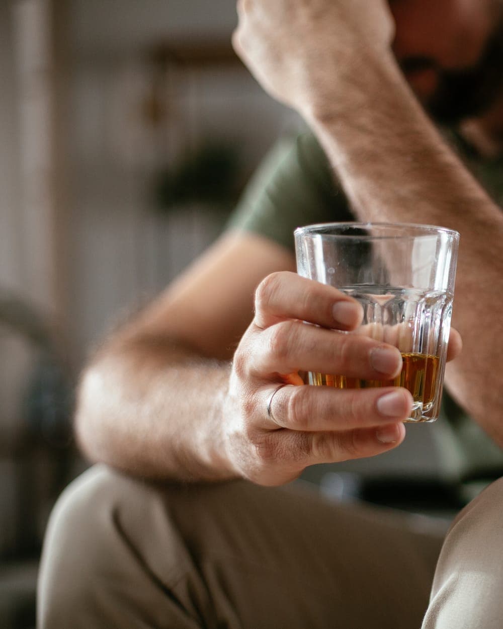 Man holding a glass of whisky, his head in his hand