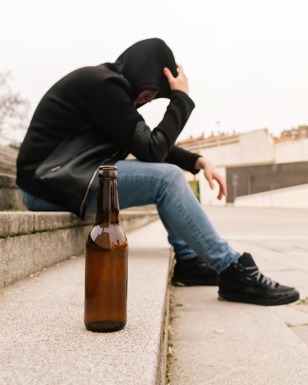 Man sitting on steps with his head in his hand, a beer bottle beside him