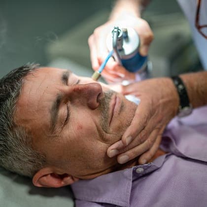 Practitioner treating a skin tag on a man's face