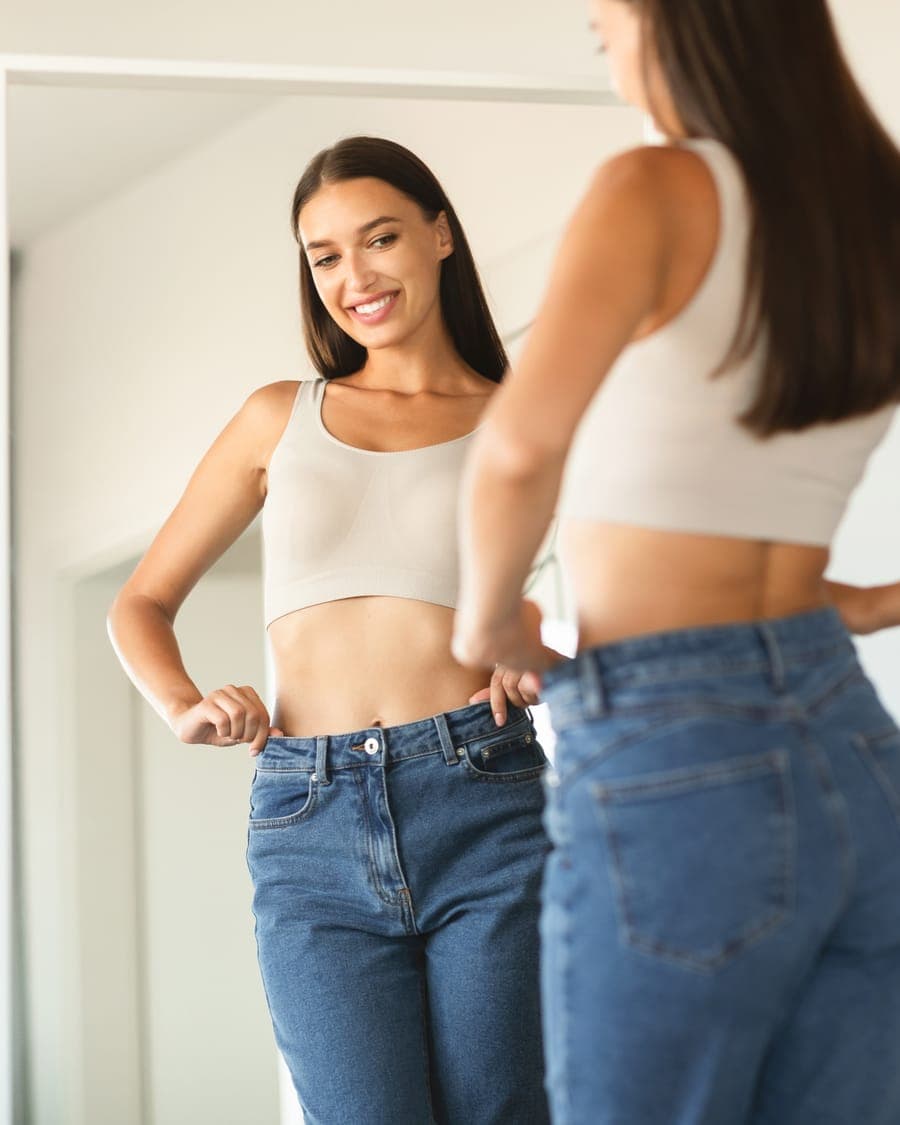 Two women in crop tops and jeans in front of a mirror