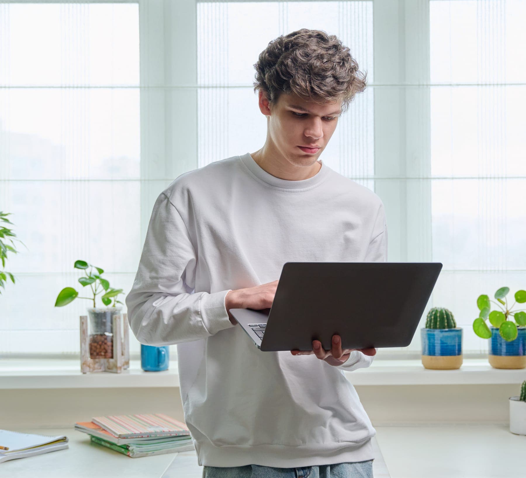 Young man at home by the window, working on a laptop