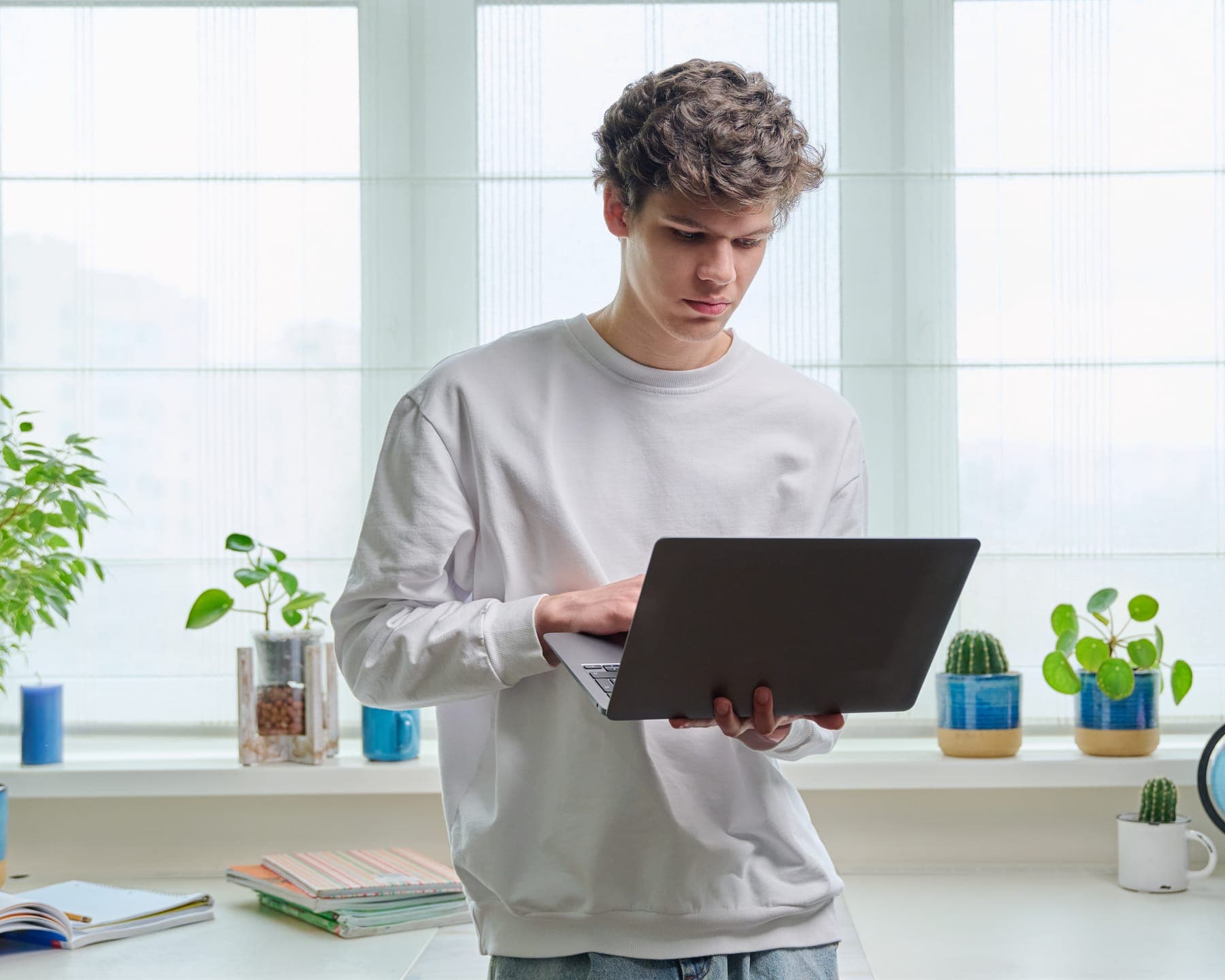 Young man at home by the window, working on a laptop