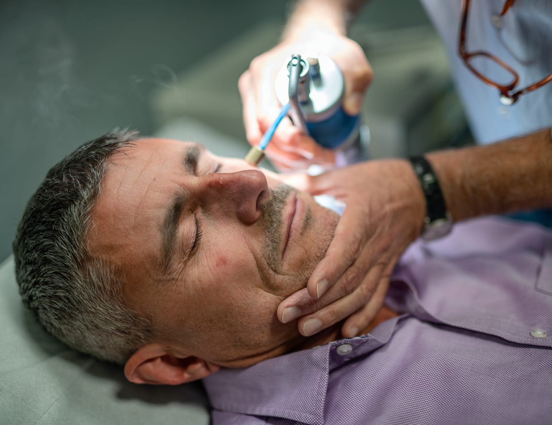 Practitioner treating a skin tag on a man's face