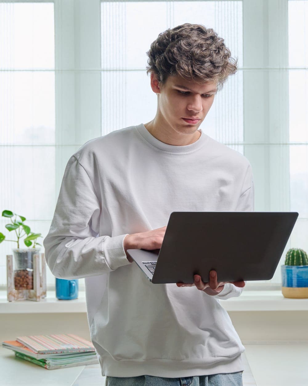 Young man at home by the window, working on a laptop